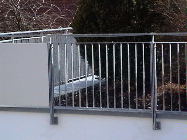 Ein Metallgeländer an einer weißen Wand mit Bäumen im Hintergrund.