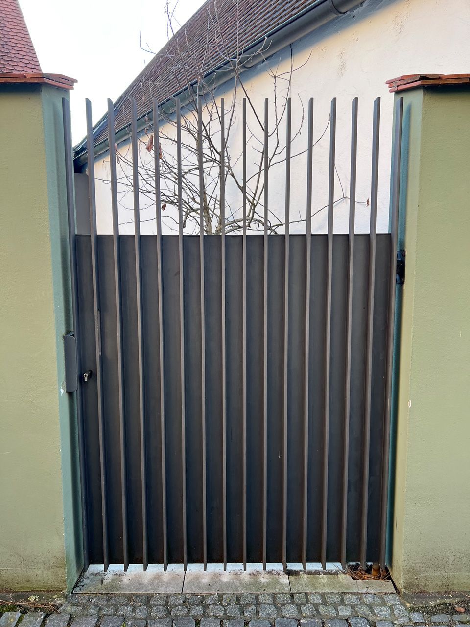 Ein Tor mit einem Zaun dahinter und einem Haus im Hintergrund.