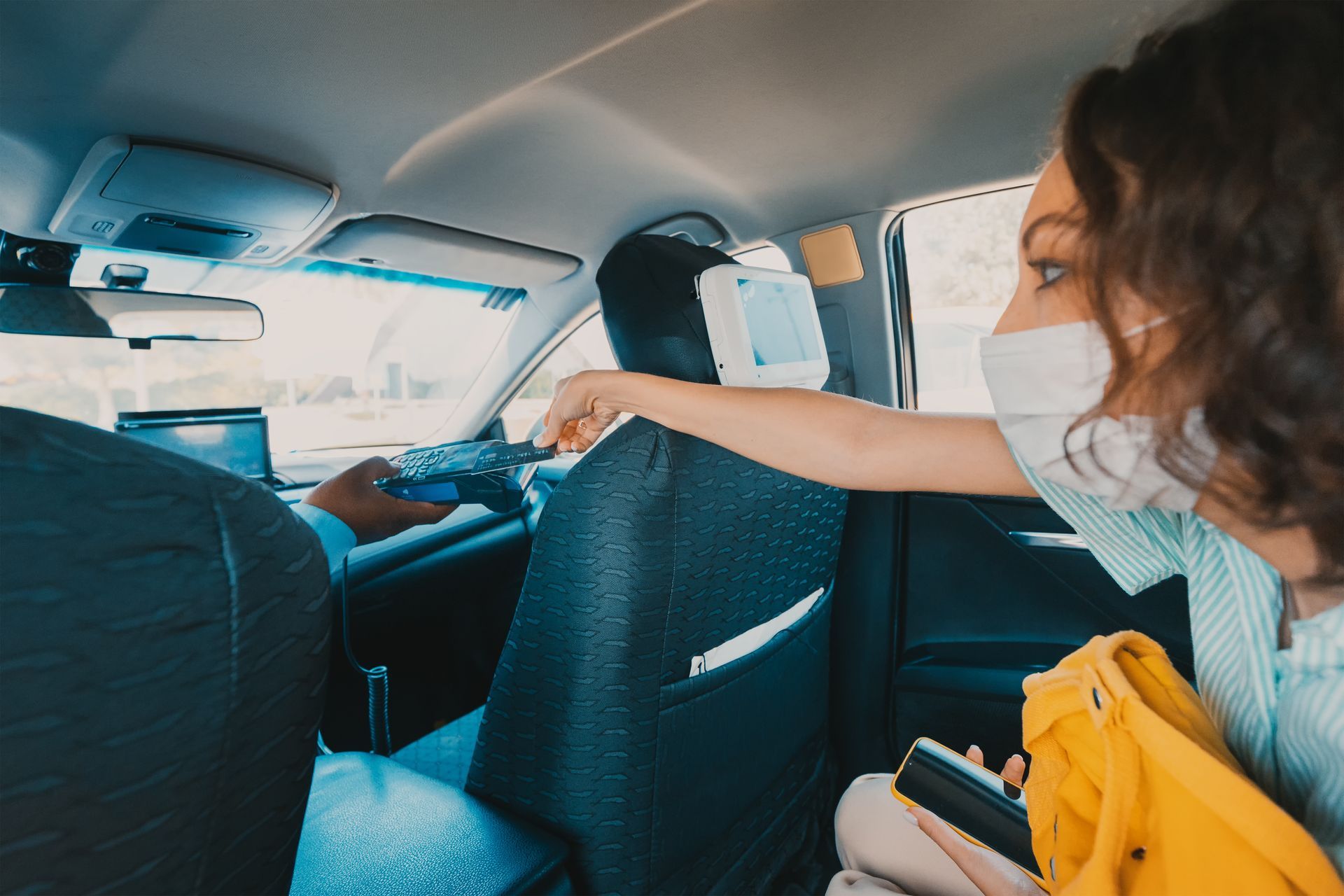 Personne avec un masque qui paie en carte bleue dans un taxi