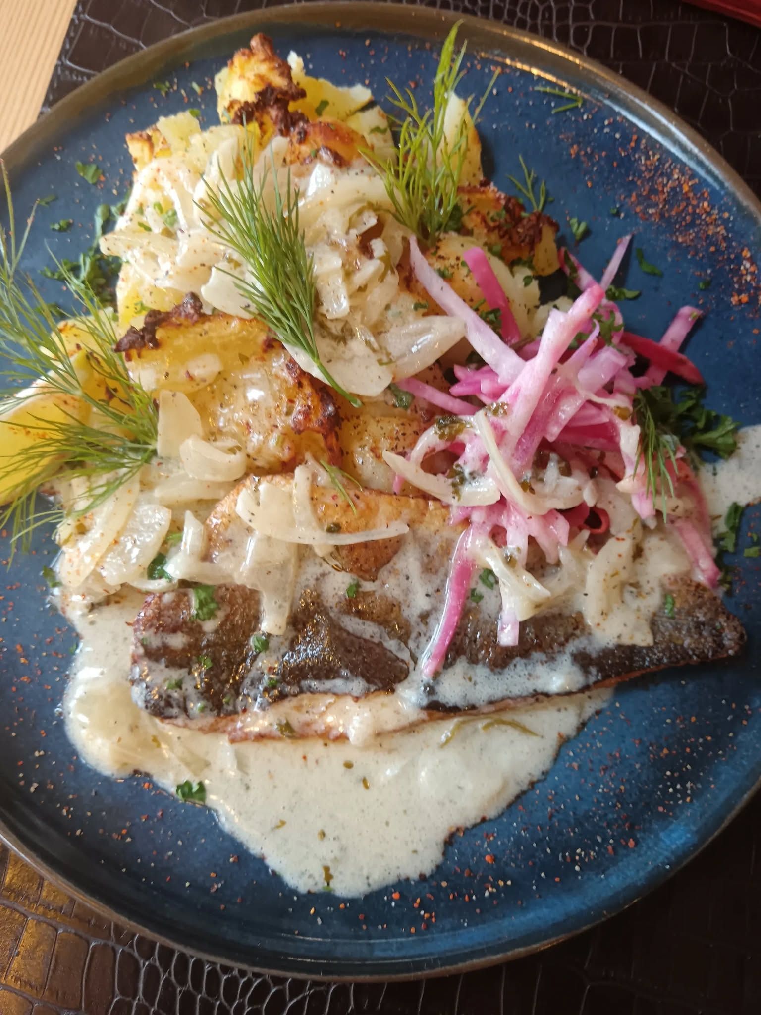 Poisson nappé d'une sauce servi avec des légumes dans une assiette bleue.