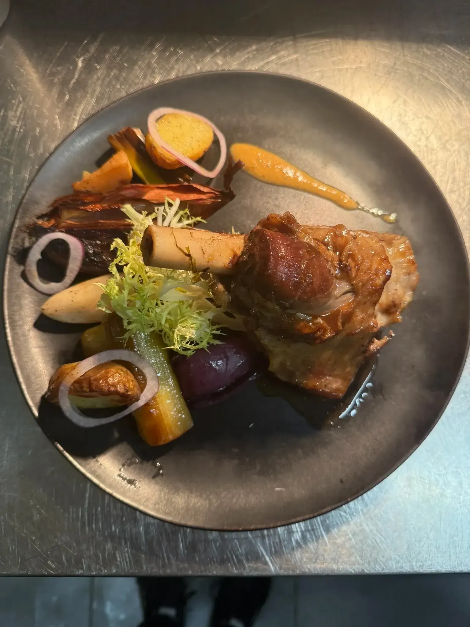 Souris d'agneau accompagnée de légumes présentée dans une assiette grise.