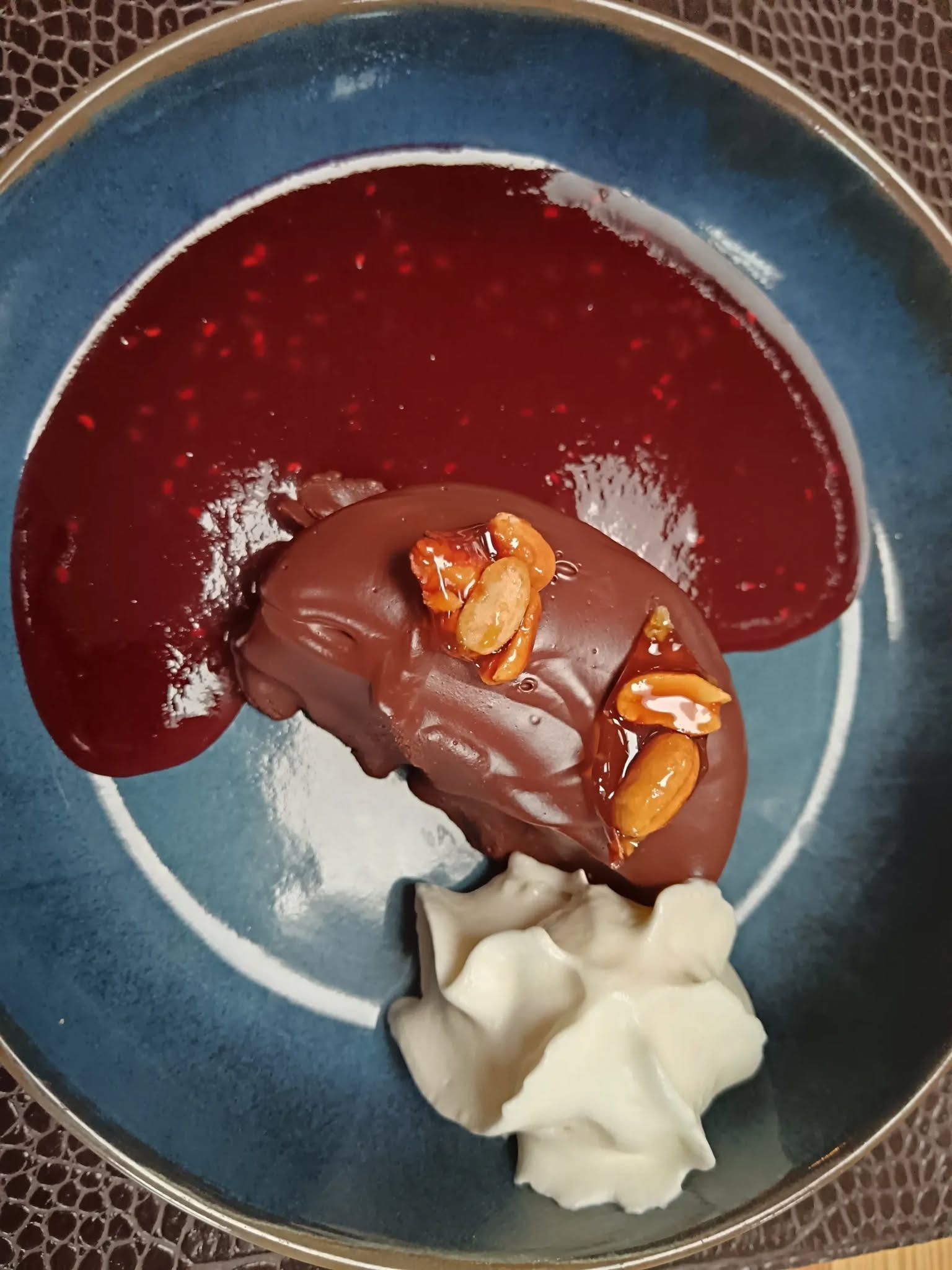 Dessert au chocolat avec coulis de fruits rouges et crème fouettée dans une assiette bleue.