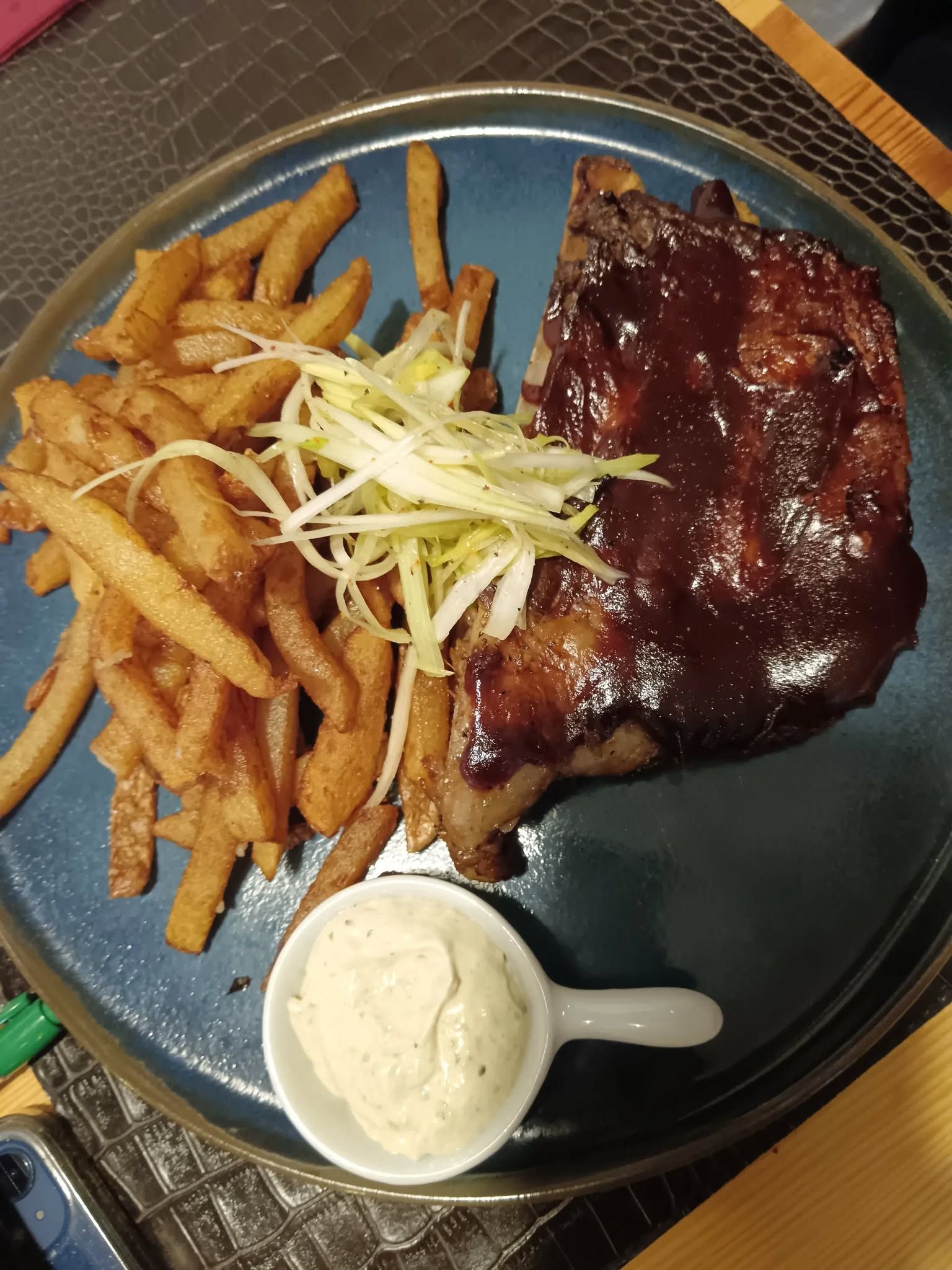 Viande grillée nappée de sauce accompagnée de frites présentée dans une assiette bleue.