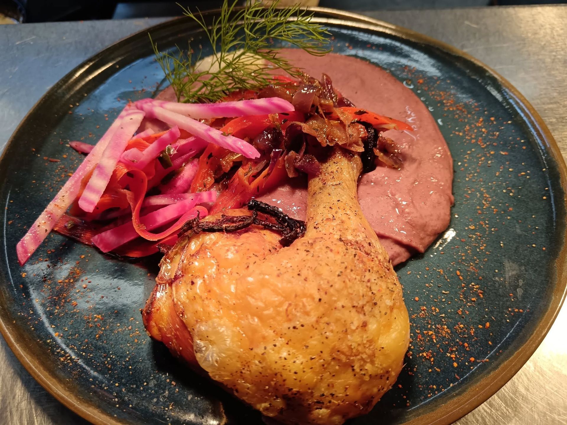 Cuisse de poulet rôtie avec une purée de légumes présenté dans une assiette bleu foncé.
