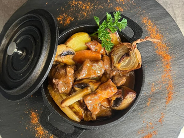 Marmite noire avec de la viande et des légumes posée sur une table grise.