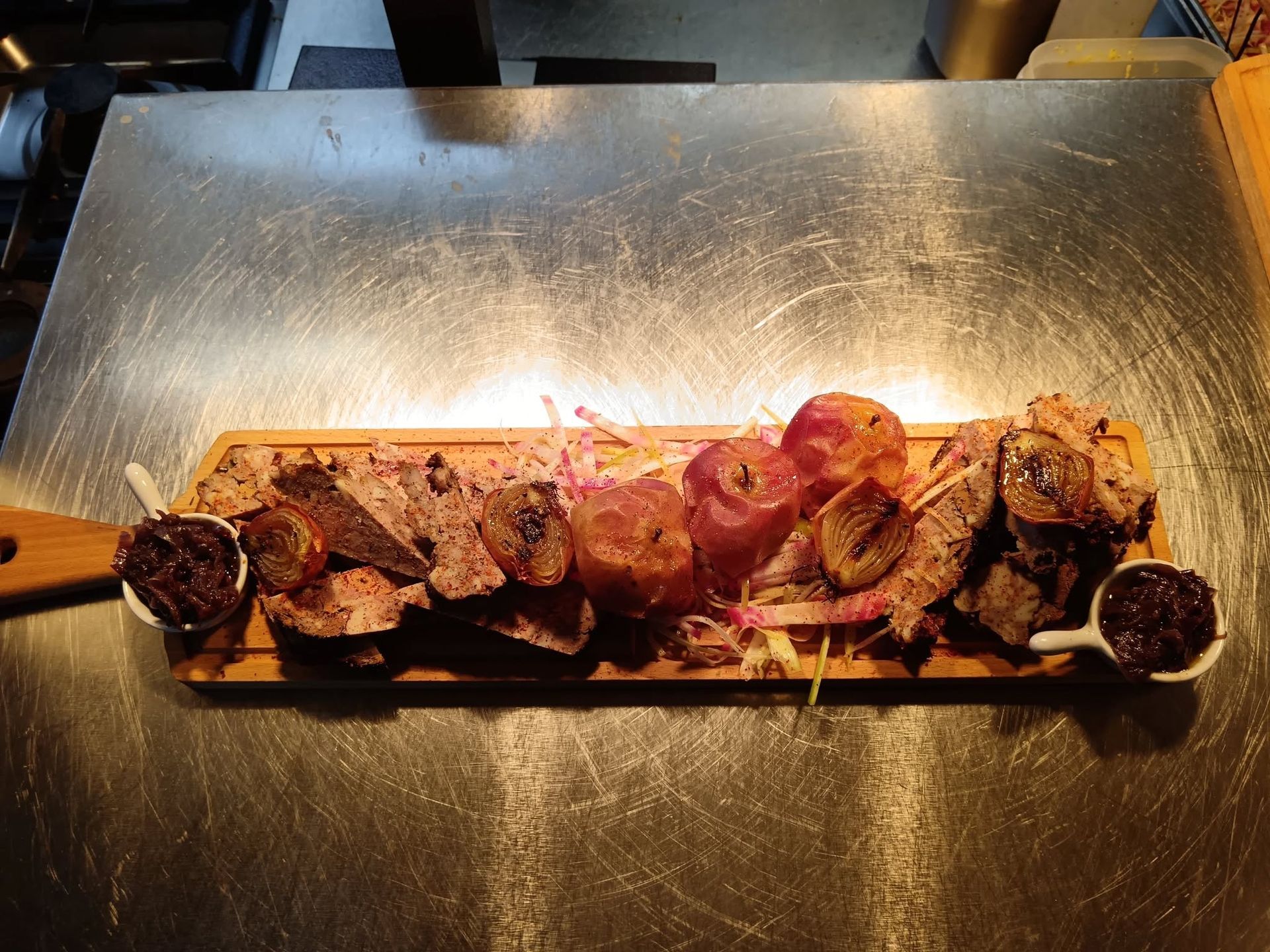 Planchette en bois avec de la charcuterie, des tomates, de la tapenade posée sur un support en aluminium.