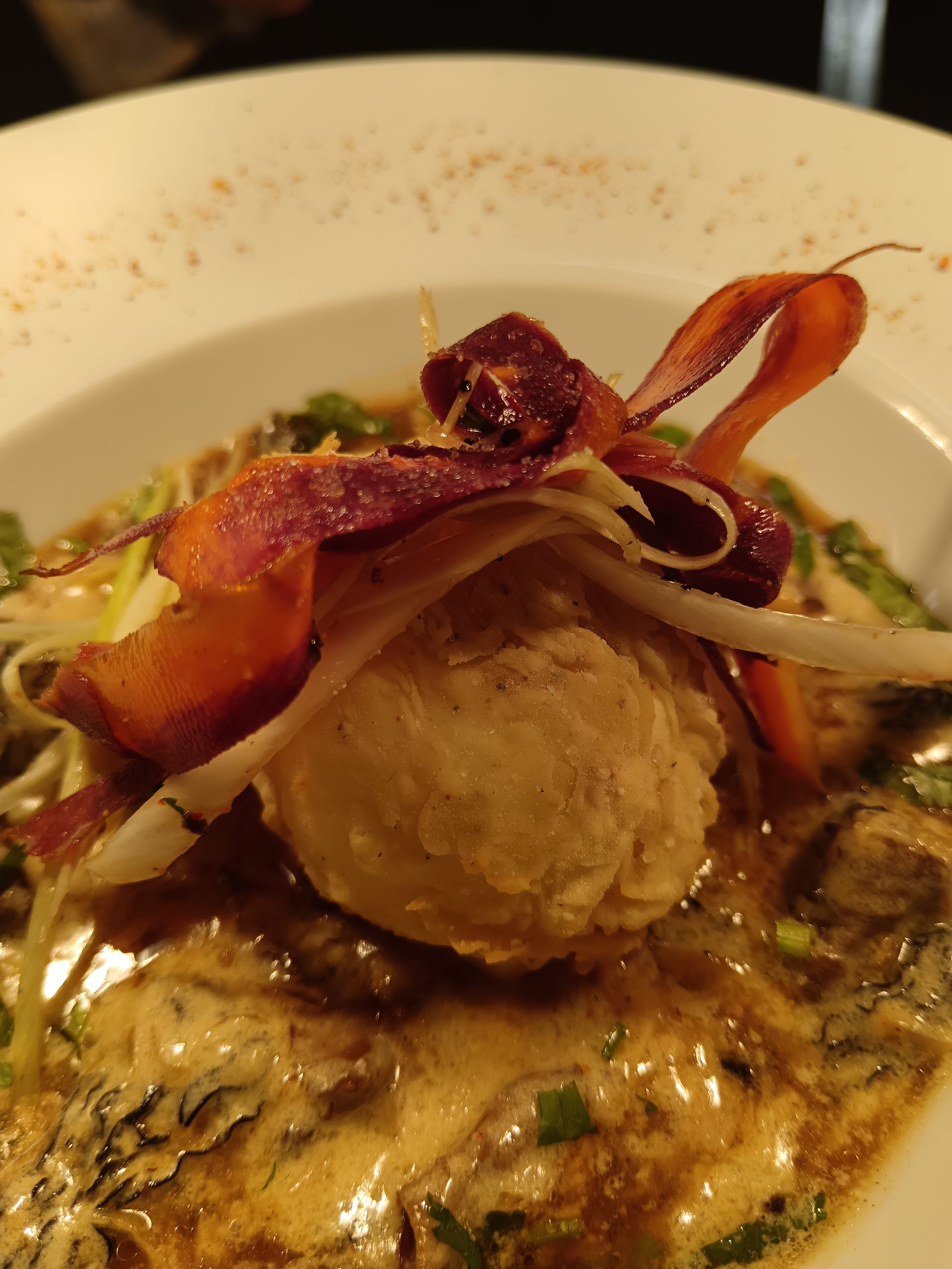 Plat gastronomique présenté sur une assiette blanche, composé d'une noix de Saint-Jacques poêlée, d'une garniture croustillante et d'une sauce.