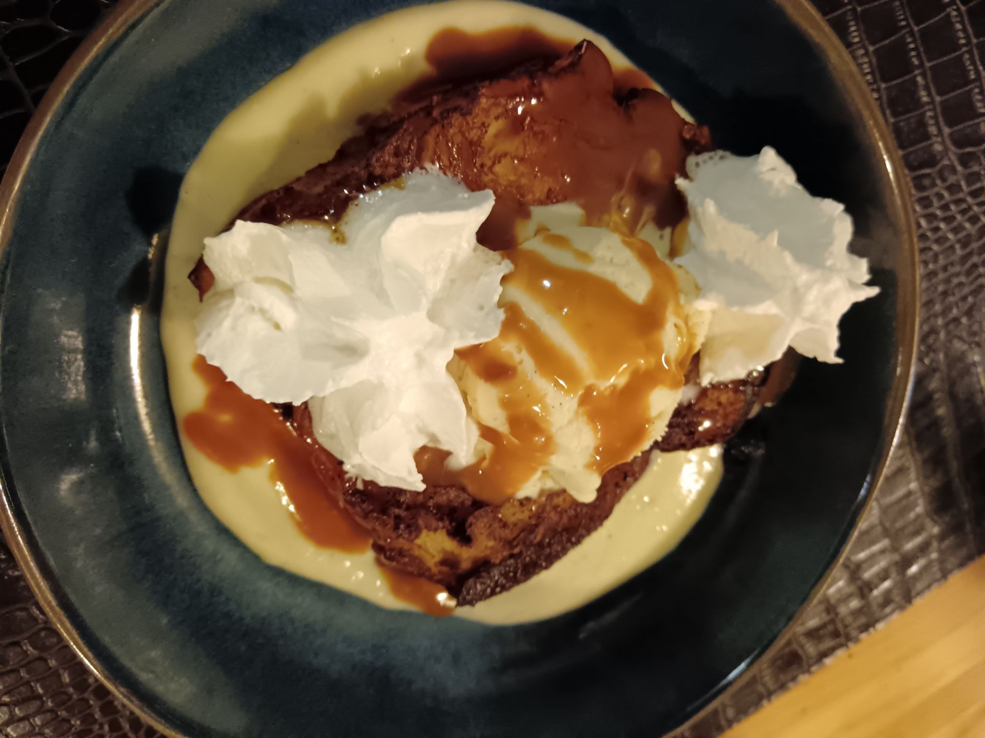 Dessert composé de crème anglaise, de sauce caramel et de crème fouettée, servi dans un bol foncé.