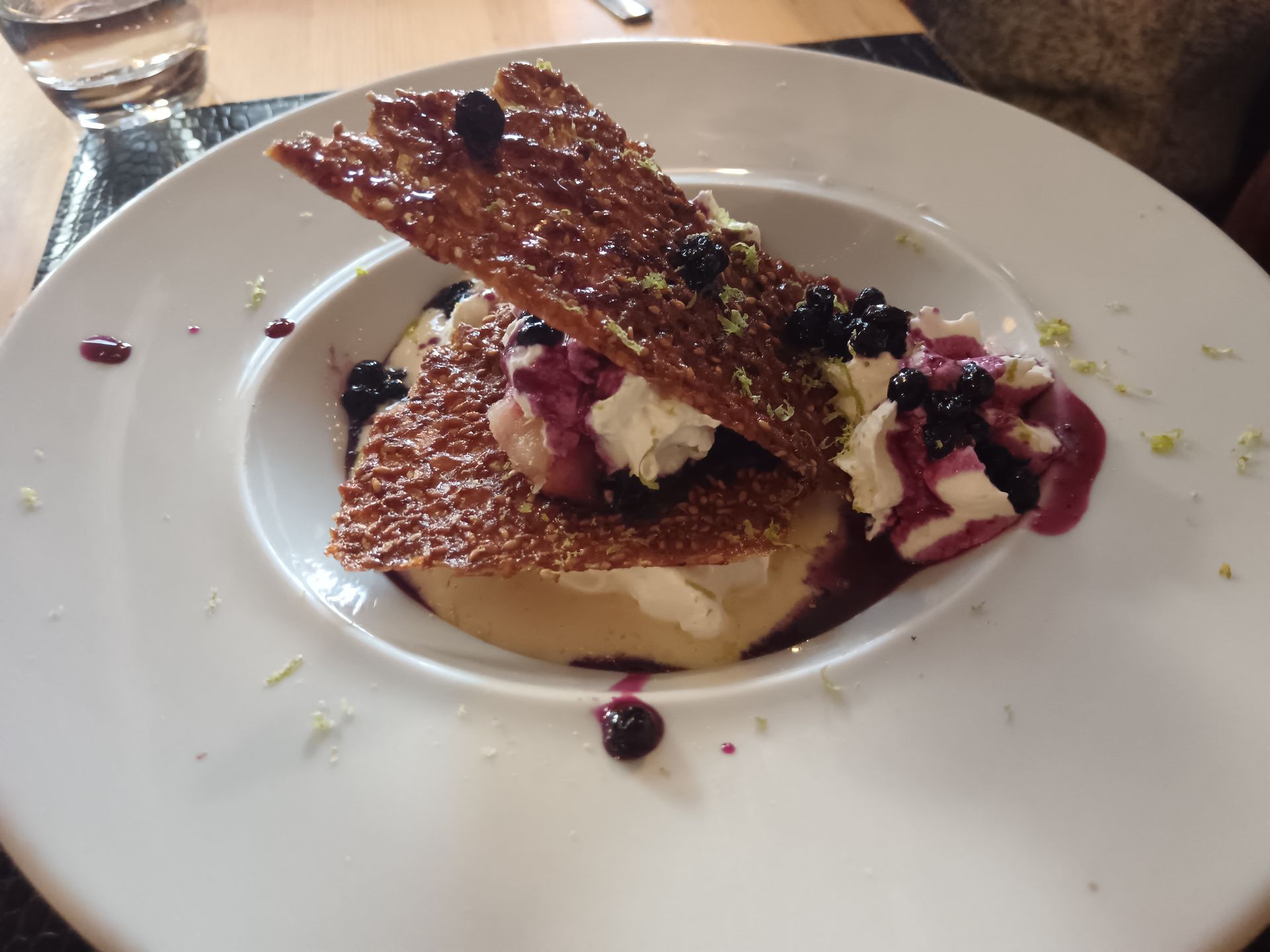 Assiette à dessert avec des triangles de pâte croustillants, de la crème et un filet de coulis de fruits rouges.
