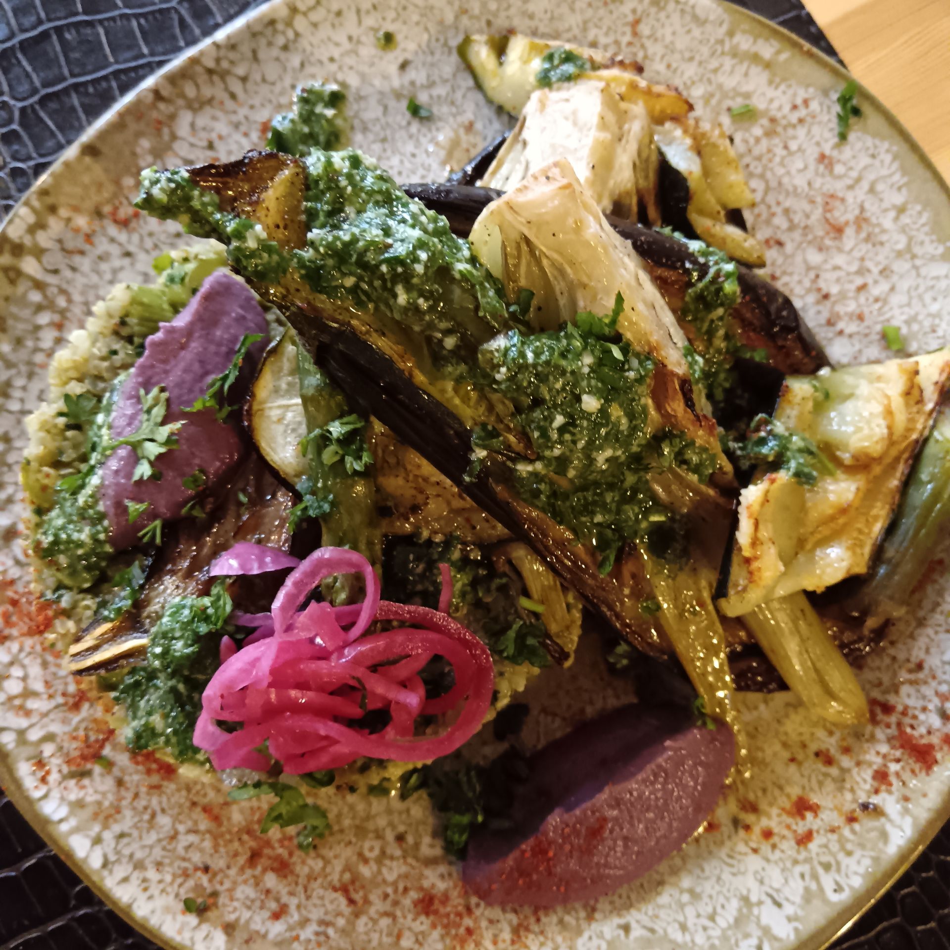 Légumes rôtis servis dans une assiette avec une sauce aux herbes et des oignons marinés.