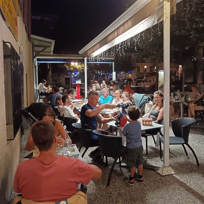Terrasse extérieure d'un restaurant avec des clients attablés sous des lumières vives la nuit