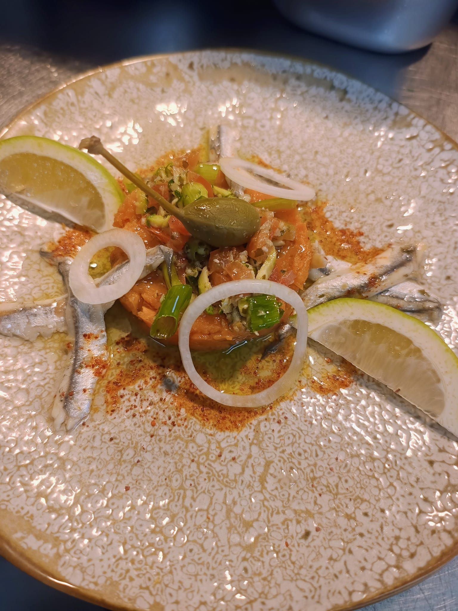 Salade gastronomique dressée sur une assiette blanche mouchetée, avec quartiers de citron vert, rondelles d'oignon et fines herbes.