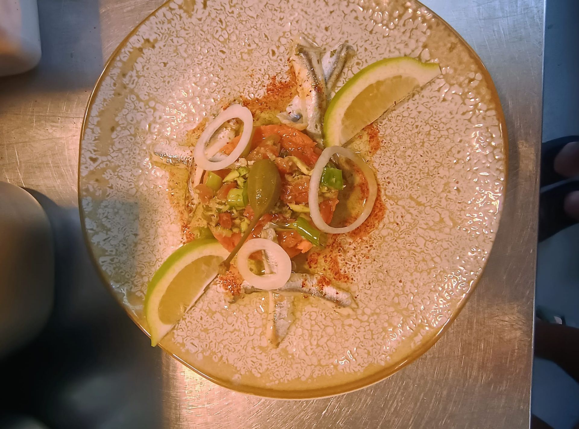 Assiette blanche avec un plat de fruits de mer composé, des quartiers de citron vert et des rondelles d'oignon vert sur une table en métal.