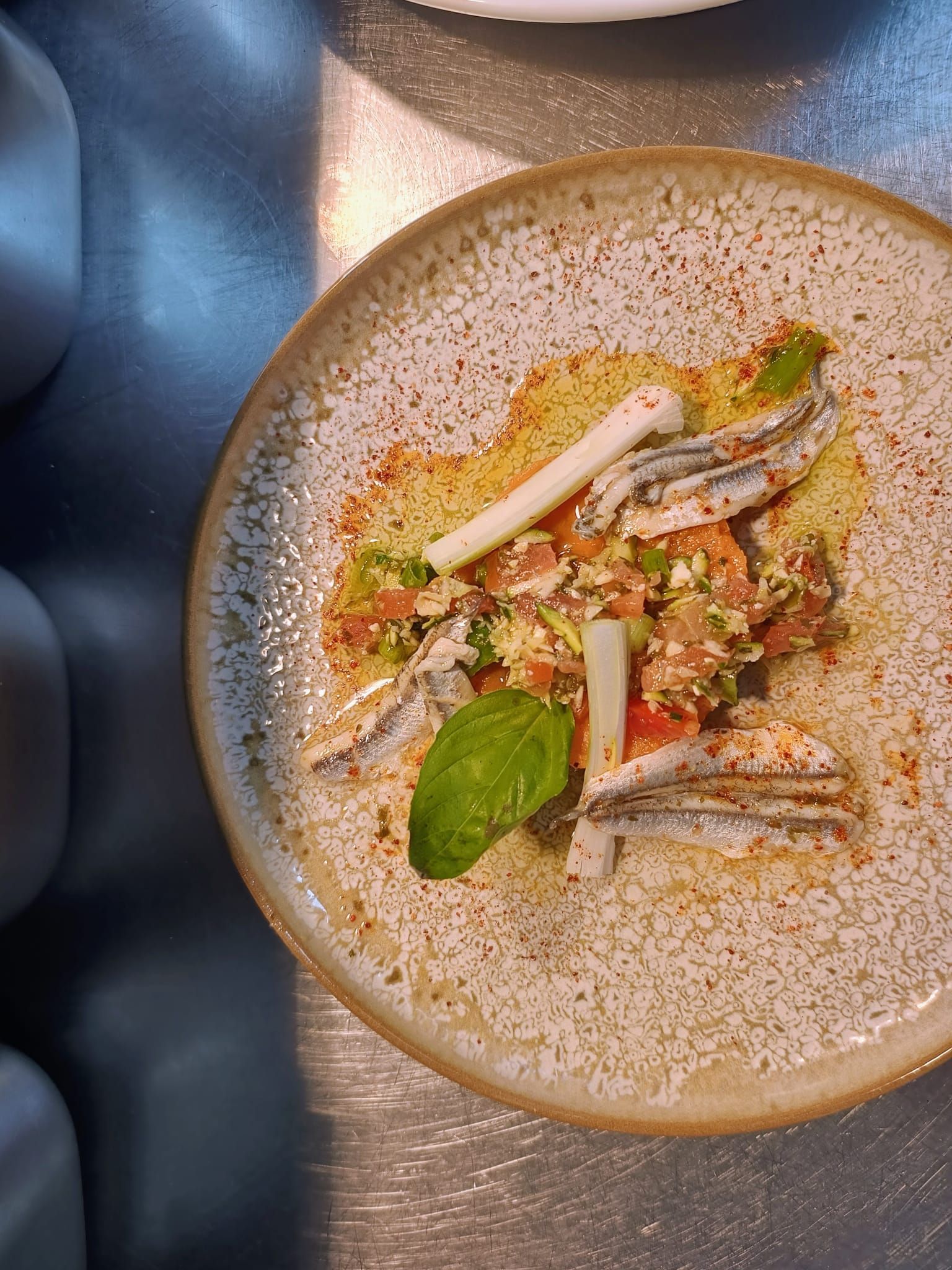 Dessert à l'assiette avec mousse blanche, garniture verte et crumble, présenté sur une table en métal