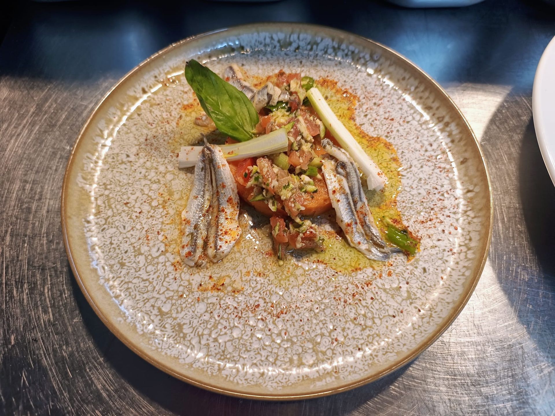 Plat gastronomique présenté dans une assiette en céramique mouchetée, composé de deux filets de poisson, de légumes verts et d'une garniture d'herbes.