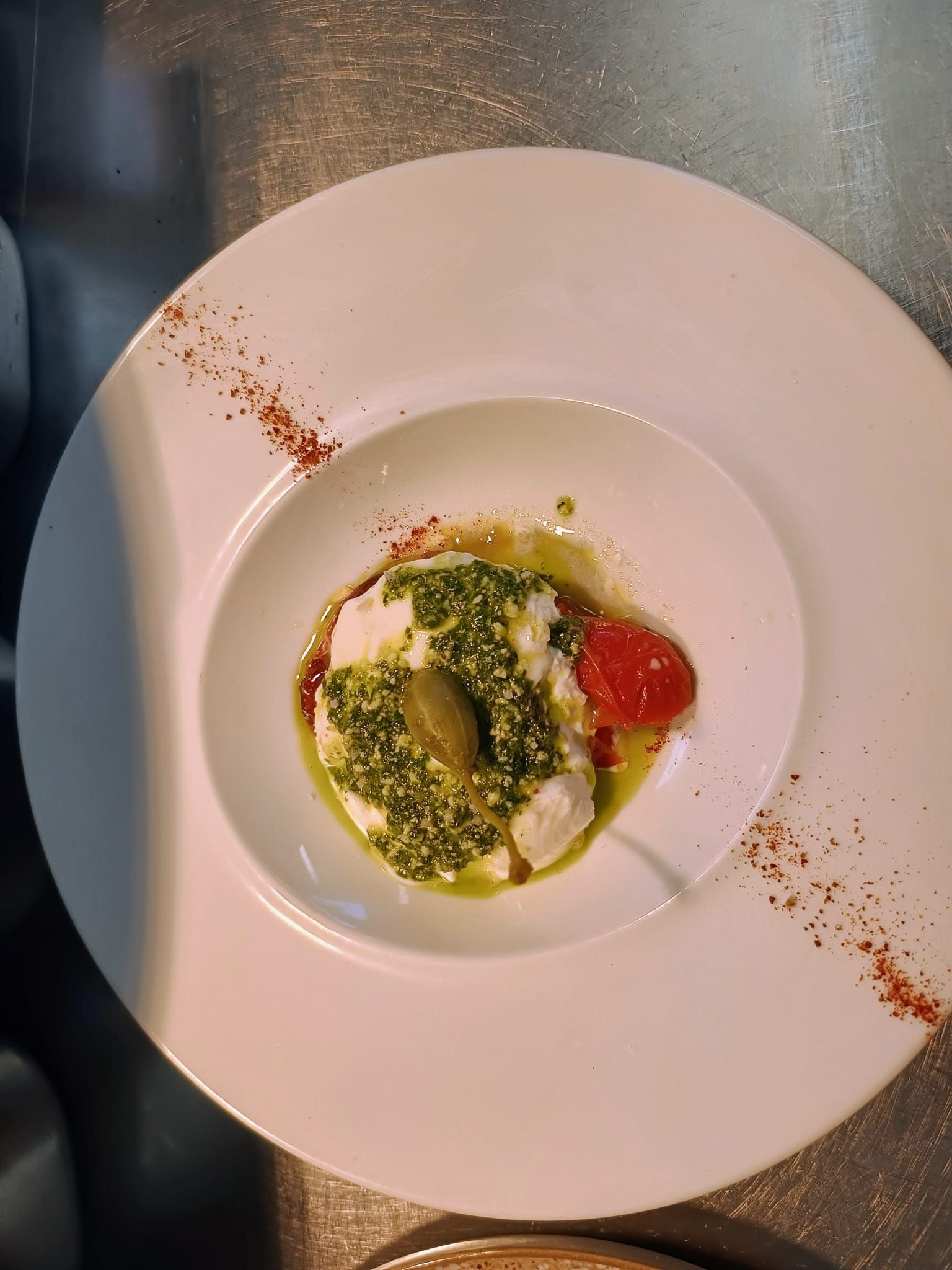 Assiette d'entrée gastronomique avec sauce verte, fromage et tomate sur un plat blanc, garnie d'un filet de sauce.