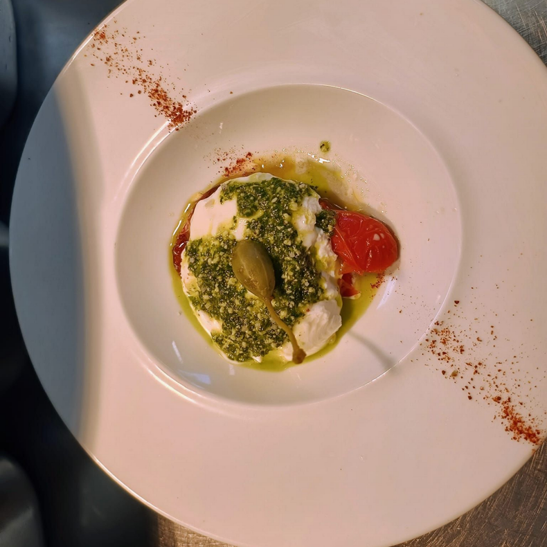 Assiette blanche avec un petit plat gastronomique, une sauce verte et une garniture rouge sur une table.
