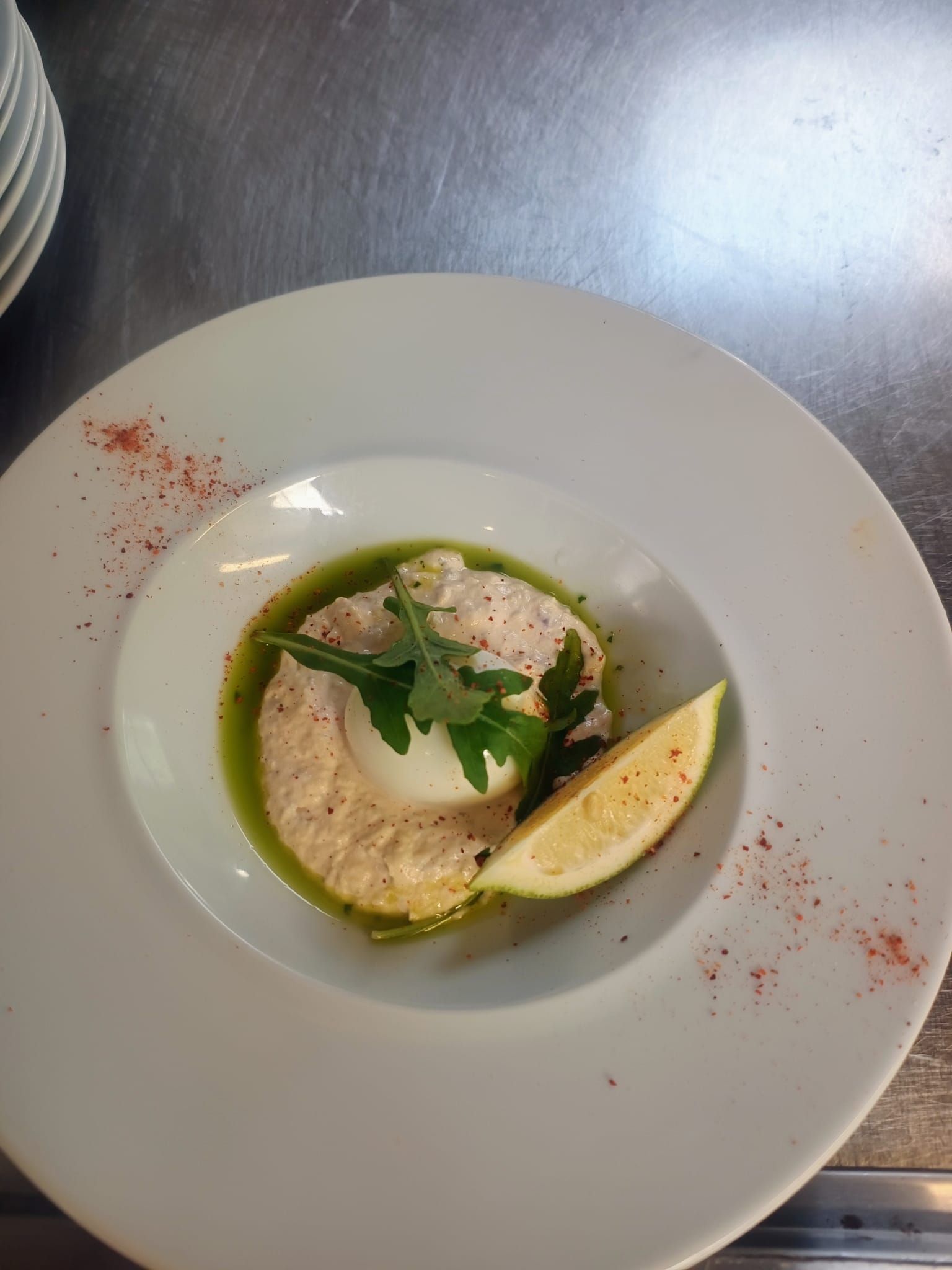Soupe crémeuse ou purée servie dans une assiette blanche, garnie d'herbes aromatiques et d'un quartier de citron, saupoudrée d'épices rouges.