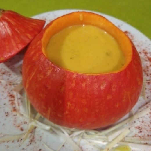 Bol en courge, rempli d'une soupe jaune crémeuse, présenté sur une assiette avec garniture.