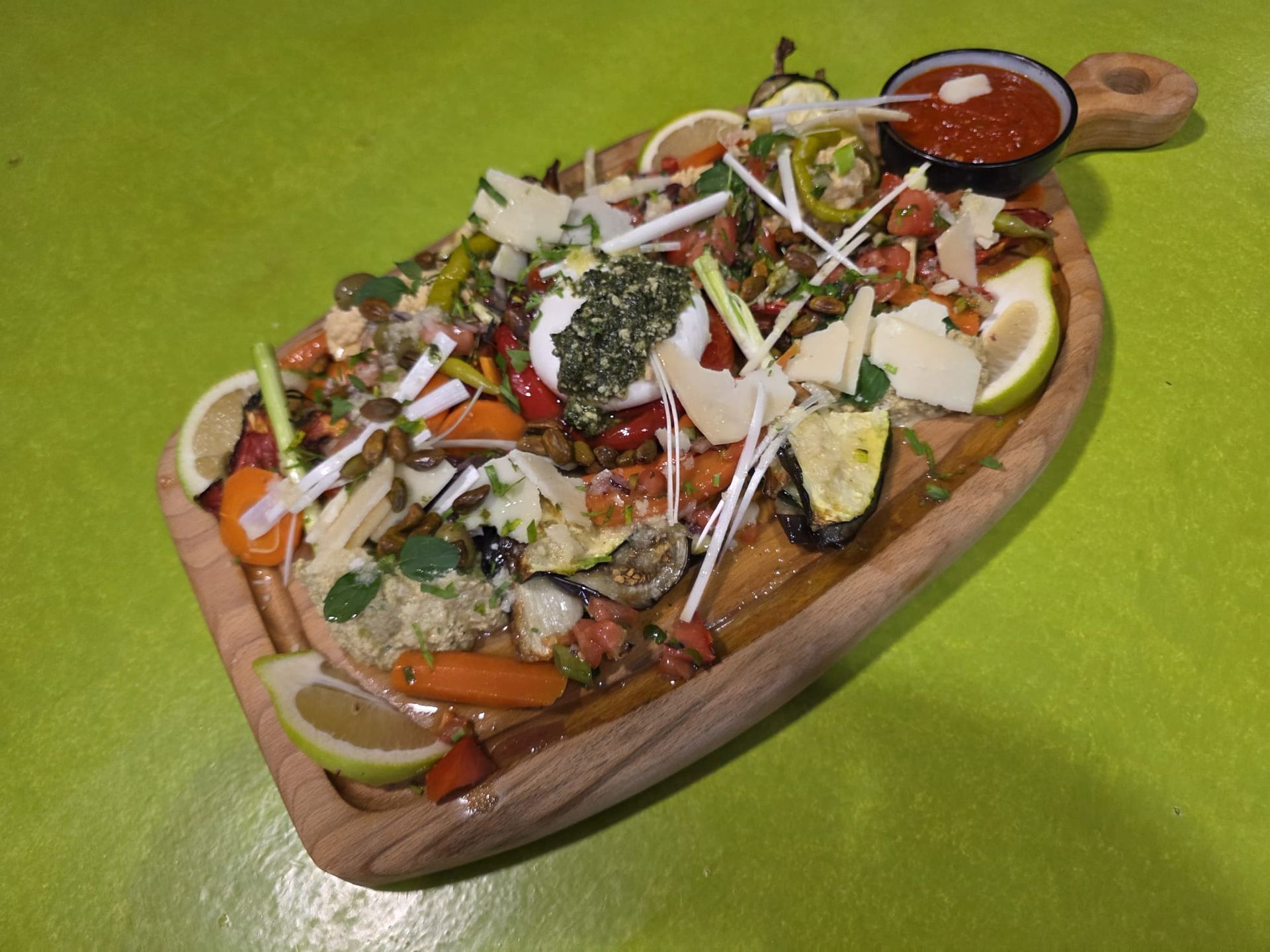 Salade composée dans un saladier en bois, avec des légumes verts, des carottes, du fromage et de la vinaigrette, posée sur une table verte.