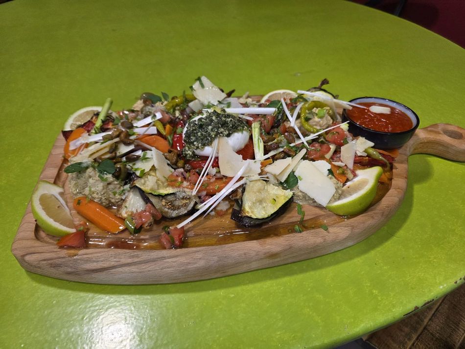 Plateau en bois garni de salade colorée et de garnitures, présenté sur une table vert vif avec une sauce pour tremper.