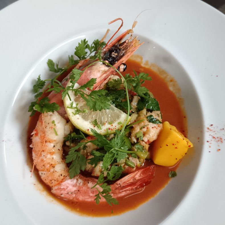 Plat de crevettes en sauce tomate aux herbes fraîches et accompagné d'un quartier de citron, servi sur une assiette blanche.