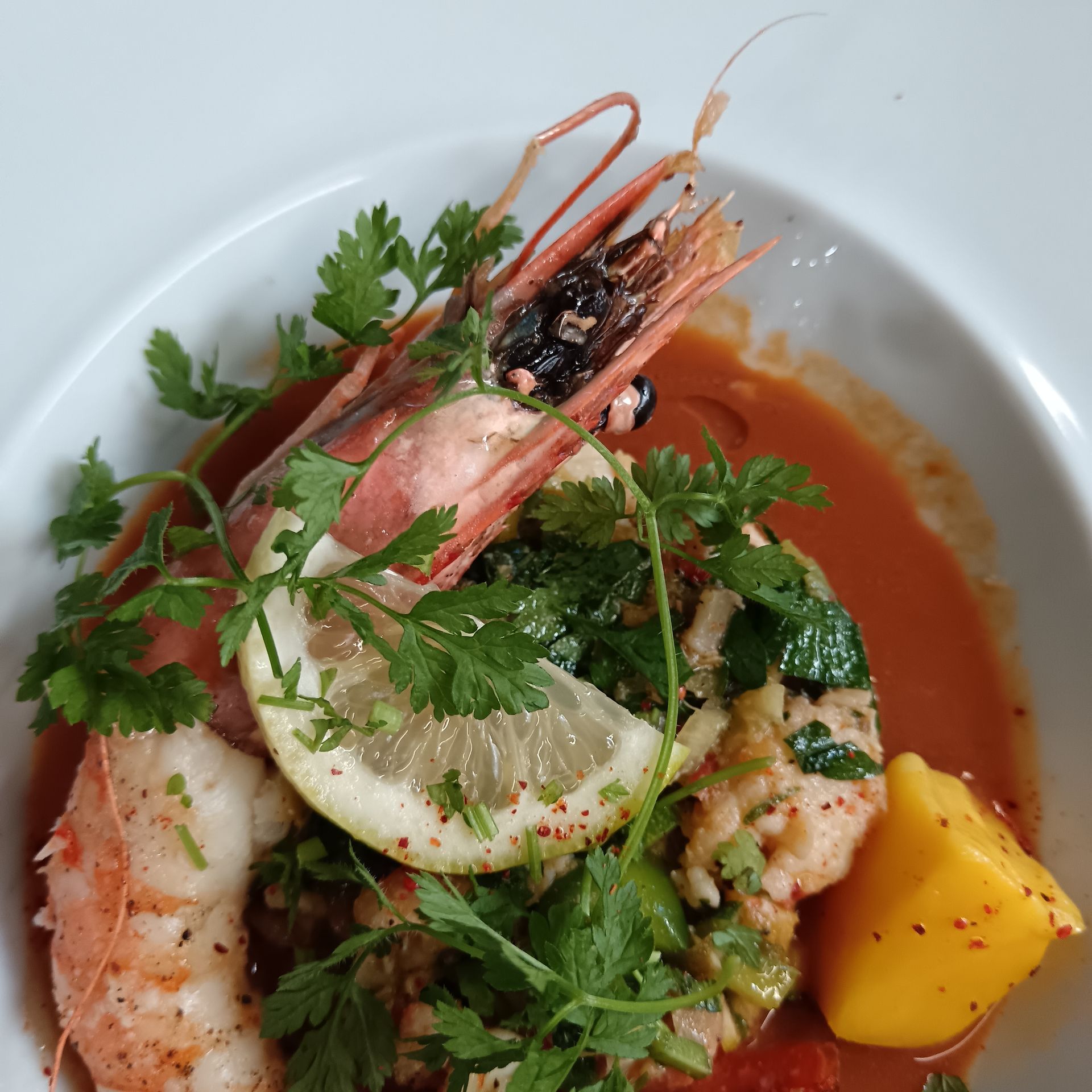Plat de fruits de mer avec crevettes, citron vert, herbes et sauce rouge sur une assiette blanche