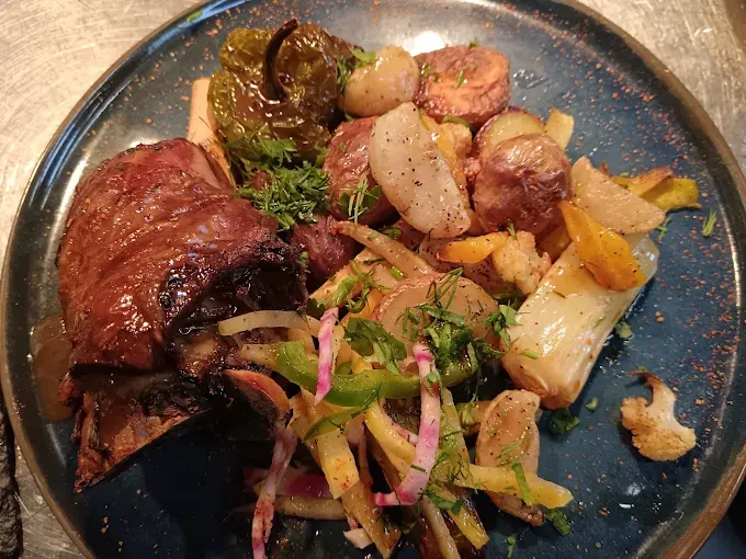 Assiette composée d'une souris d'agneau, de pommes de terre et de légumes verts.
