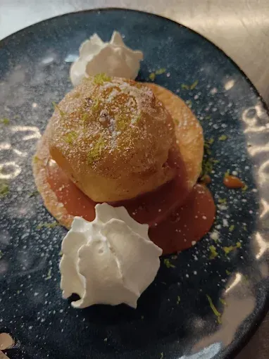 Choux à la crème servi sur une assiette bleue avec du sucre glace et des quenelles de crème fouettée.