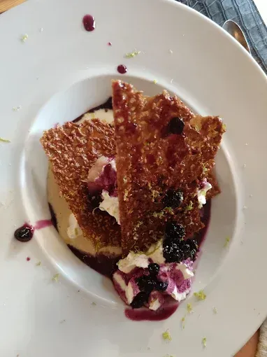 Deux tranches fines croquantes avec de la crème et un coulis aux fruits rouges dans une assiette blanche.