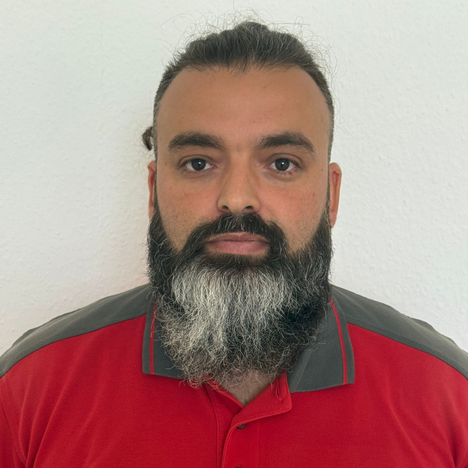 Ein glatzköpfiger Mann mit Brille und Schnurrbart trägt einen roten Pullover