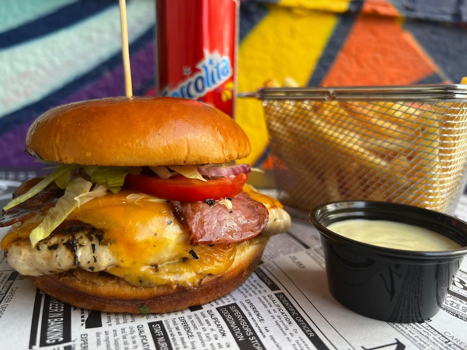 Una hamburguesa está sobre un periódico al lado de una canasta de papas fritas.