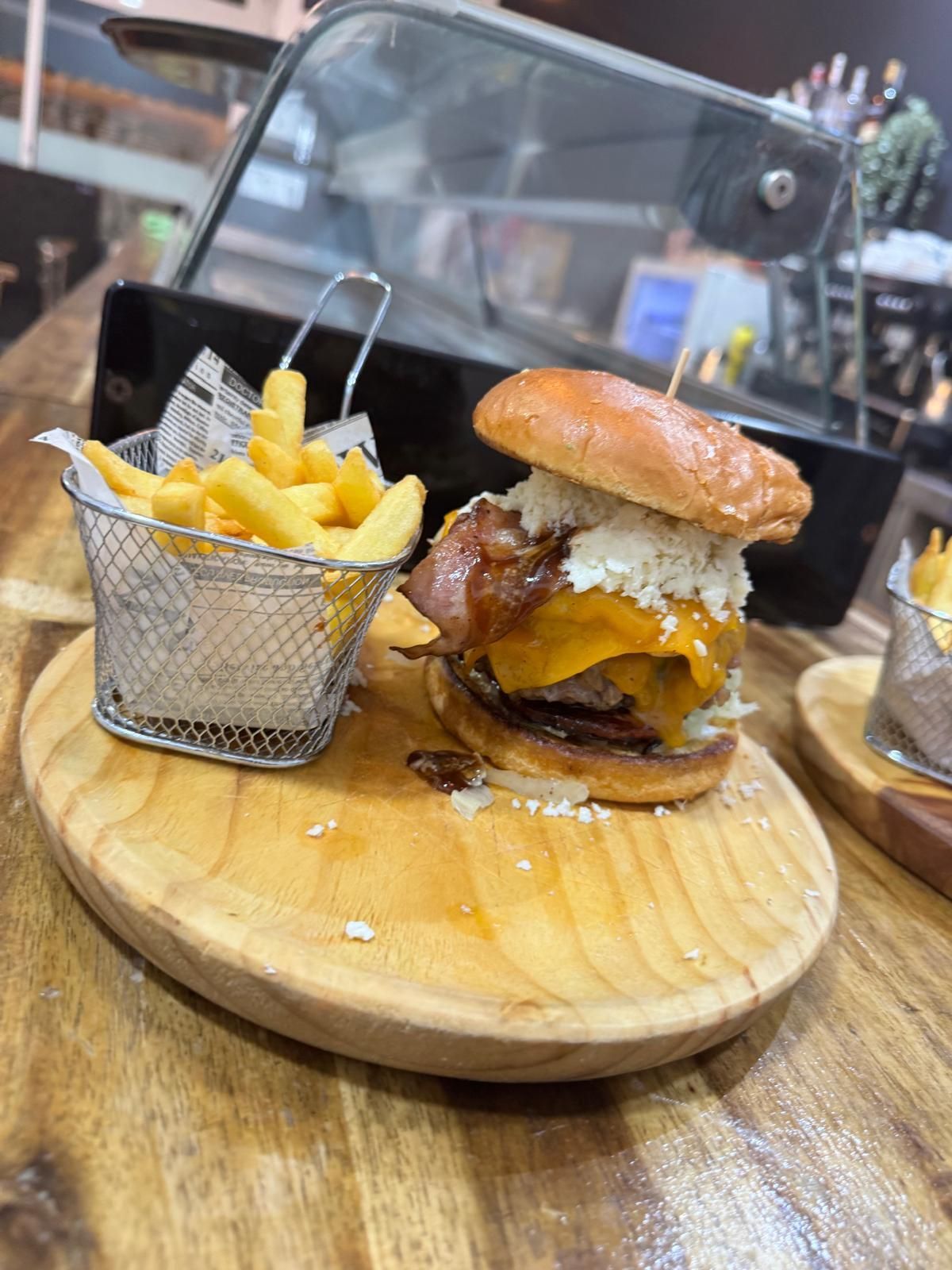Una hamburguesa y papas fritas están en una tabla de cortar de madera.