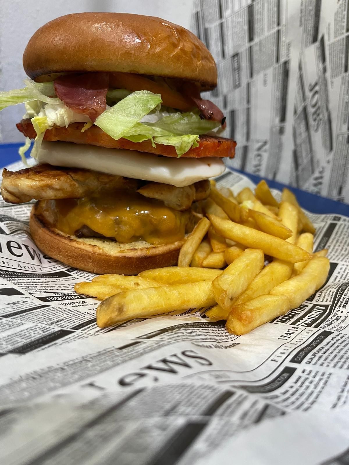 Una hamburguesa y unas patatas fritas están sobre un periódico.
