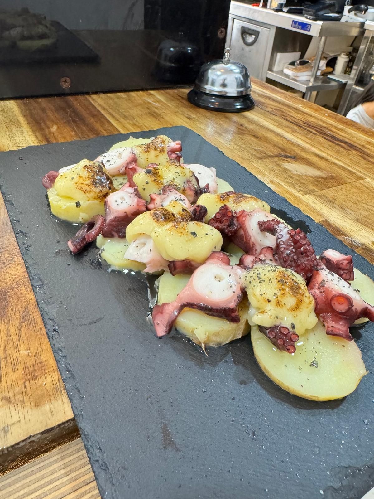 Un plato de comida con pulpo y patatas sobre una mesa de madera.