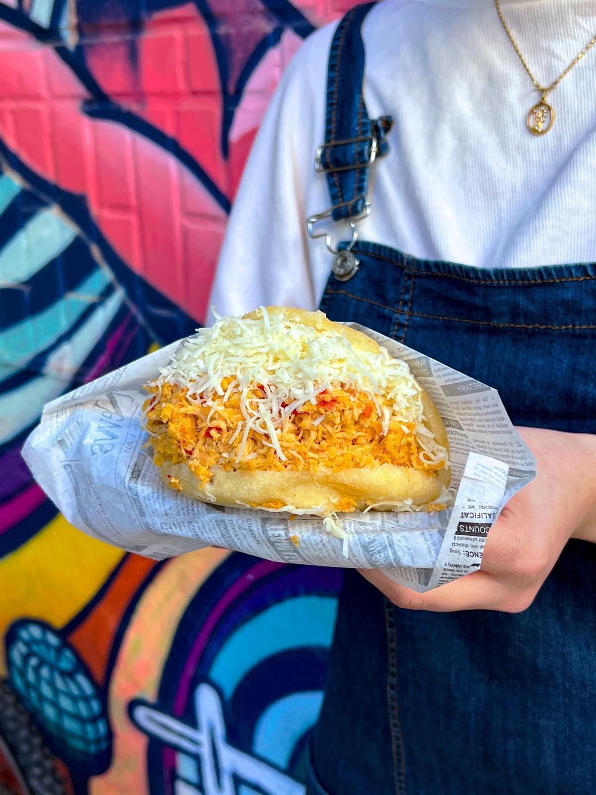 Una persona sostiene un sándwich frente a una pared con grafitis.