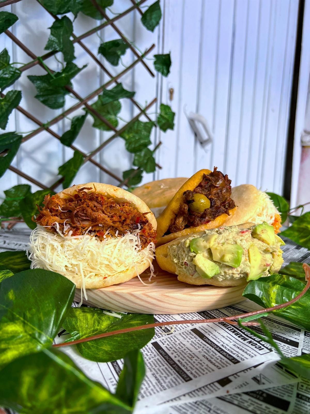 Tres arepas con diferentes ingredientes están colocadas sobre una tabla de cortar de madera encima de un periódico.