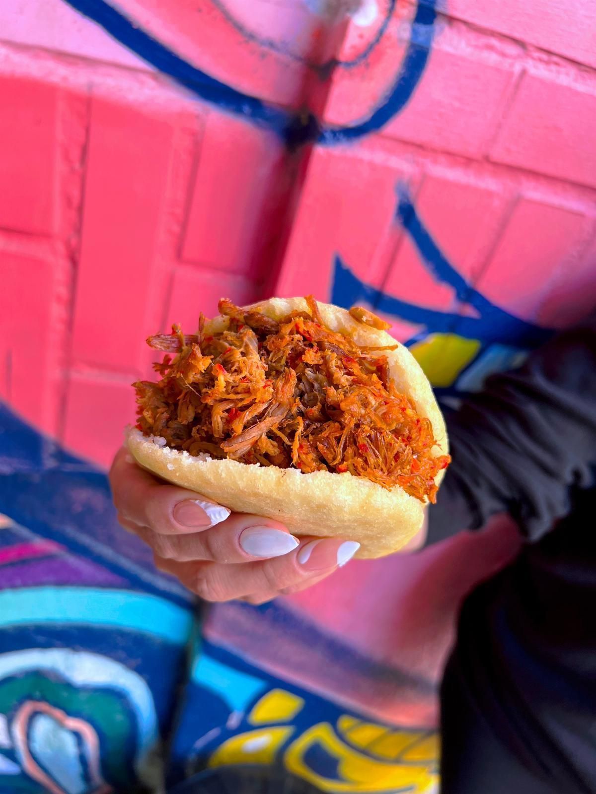Una persona sostiene un sándwich frente a una pared rosa.
