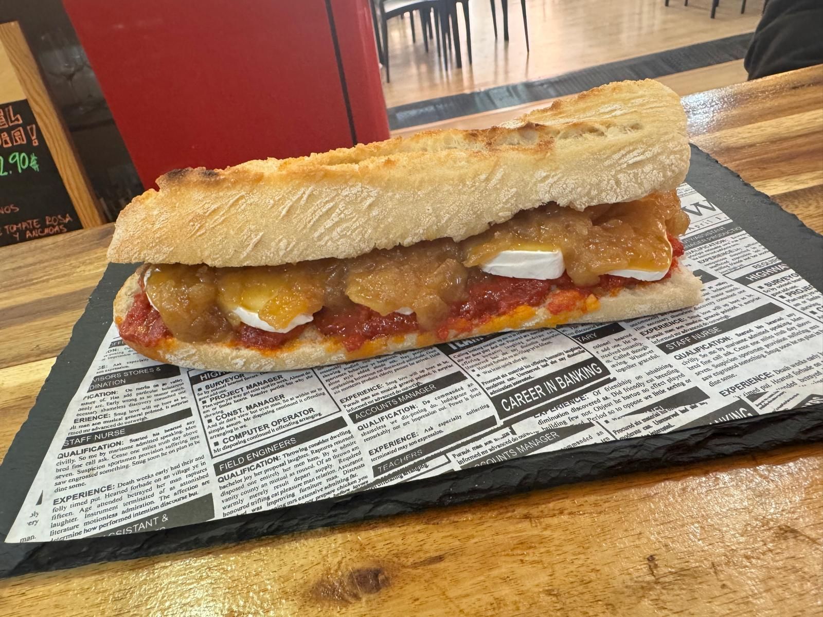Un sándwich está sobre un periódico en una mesa de madera.