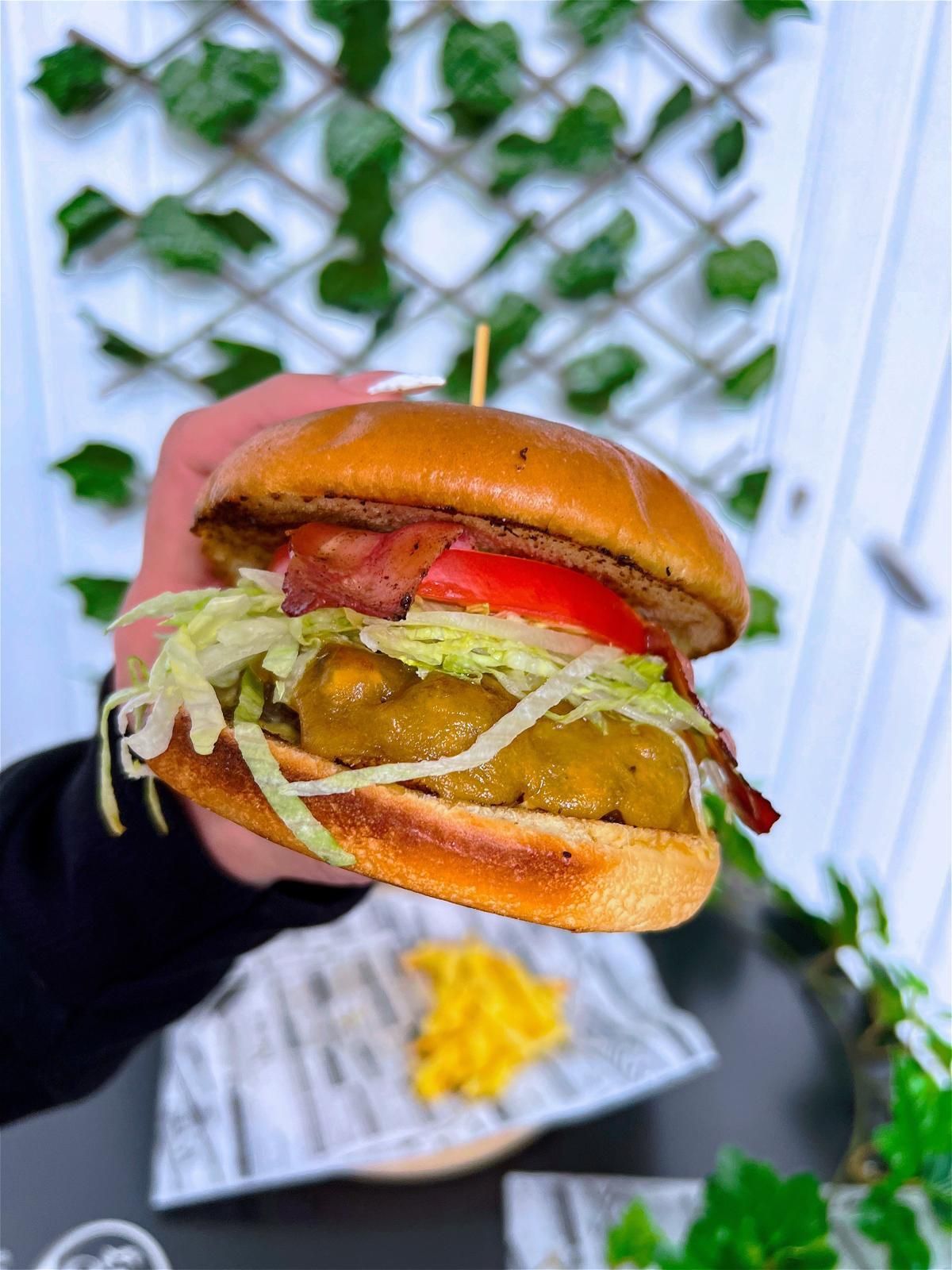 Una persona sostiene una hamburguesa con lechuga, tomate y tocino.