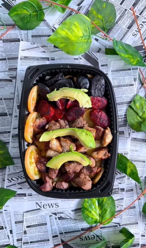 Un recipiente de plástico negro lleno de fruta y carne está encima de un periódico.
