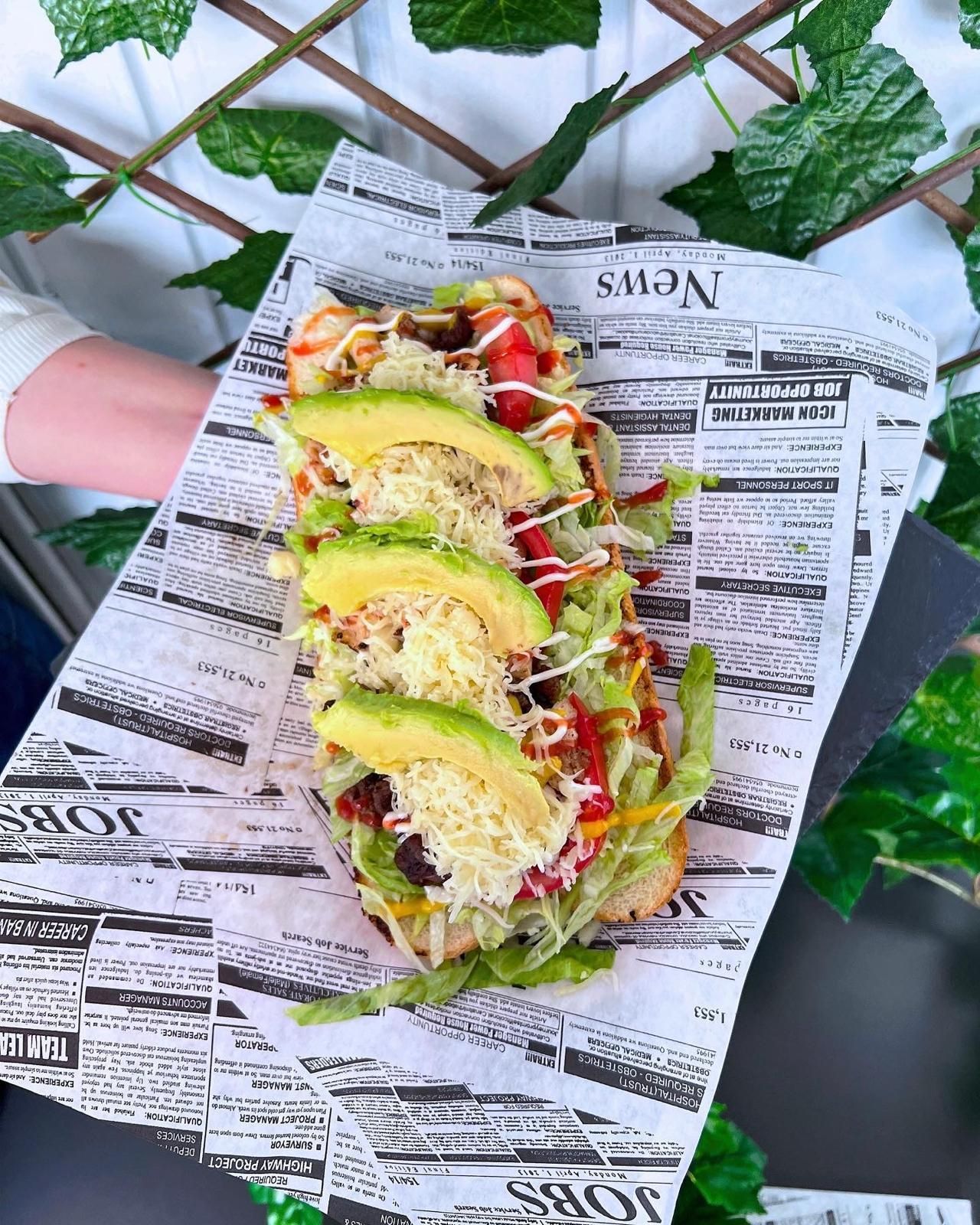 Una persona sostiene un sándwich largo sobre un trozo de periódico.