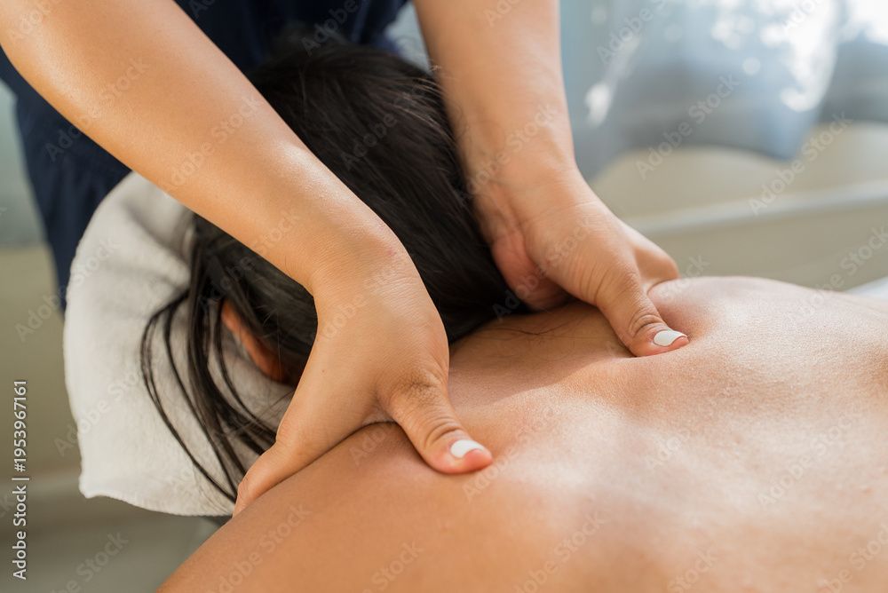 Hände drücken während einer Massage auf den nackten Rücken einer Person, im Hintergrund eine verschwommene Spa-Kulisse.