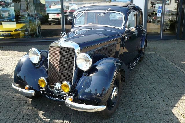 Ein altes schwarzes Auto steht vor einem Autohaus