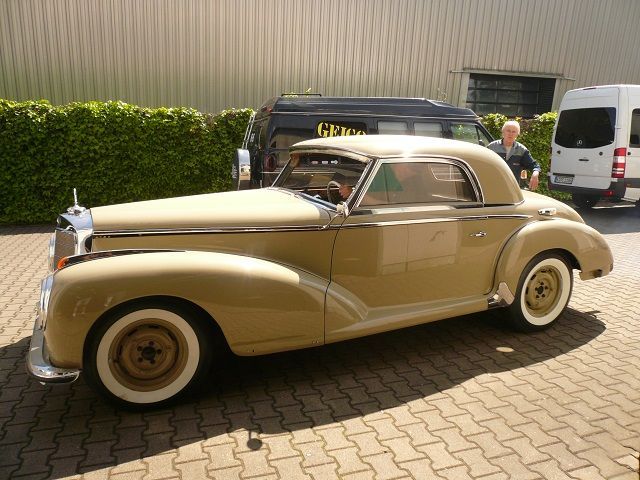 Ein hellbraunes Auto mit weißen Reifen steht auf einer gepflasterten Auffahrt