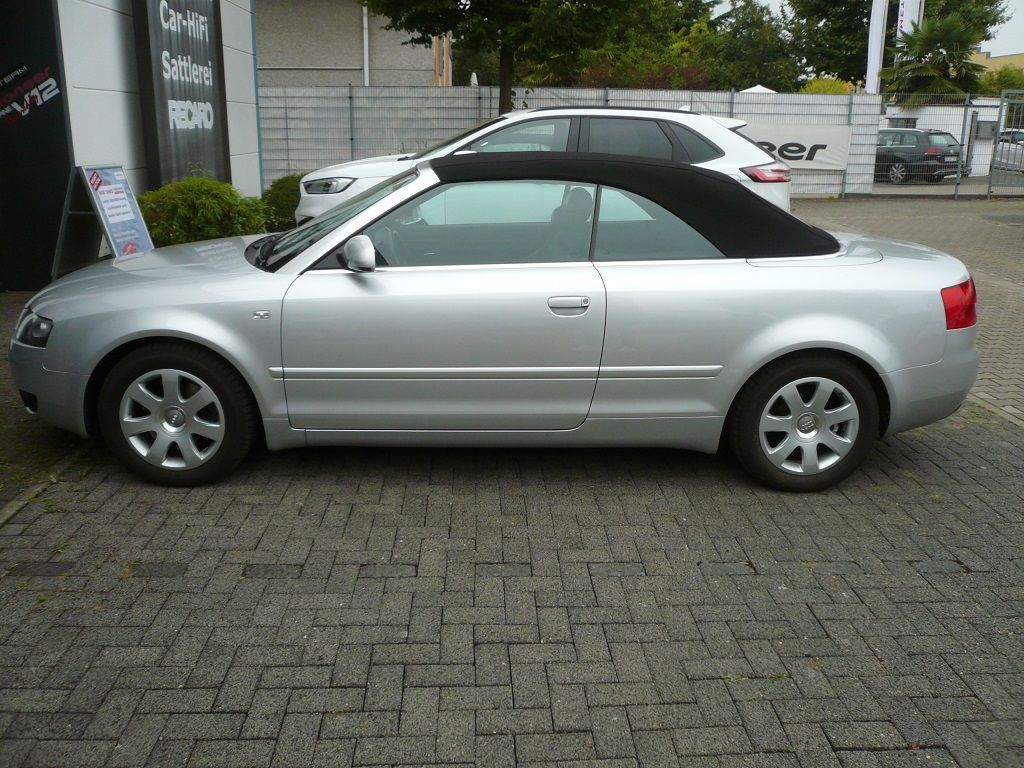 Ein silbernes Auto mit schwarzem Dach steht auf einer gepflasterten Auffahrt