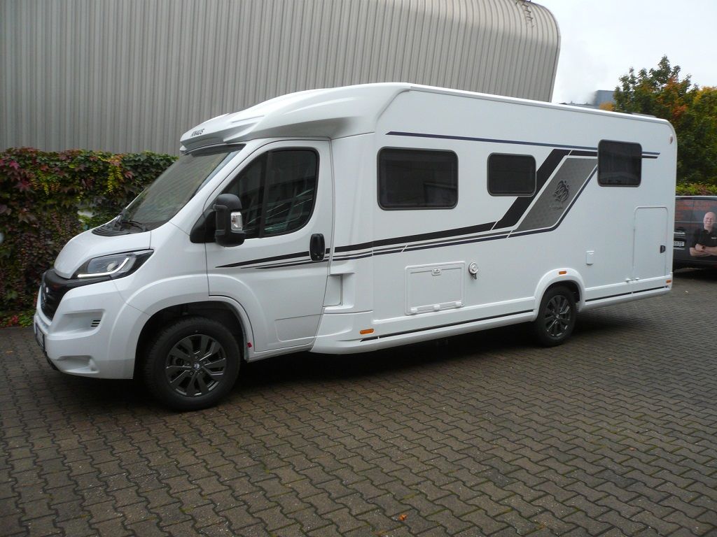 Ein weißes Wohnmobil steht auf einer gepflasterten Auffahrt vor einem Gebäude.