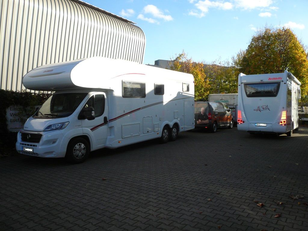 Zwei weiße Wohnmobile stehen nebeneinander auf einem Parkplatz