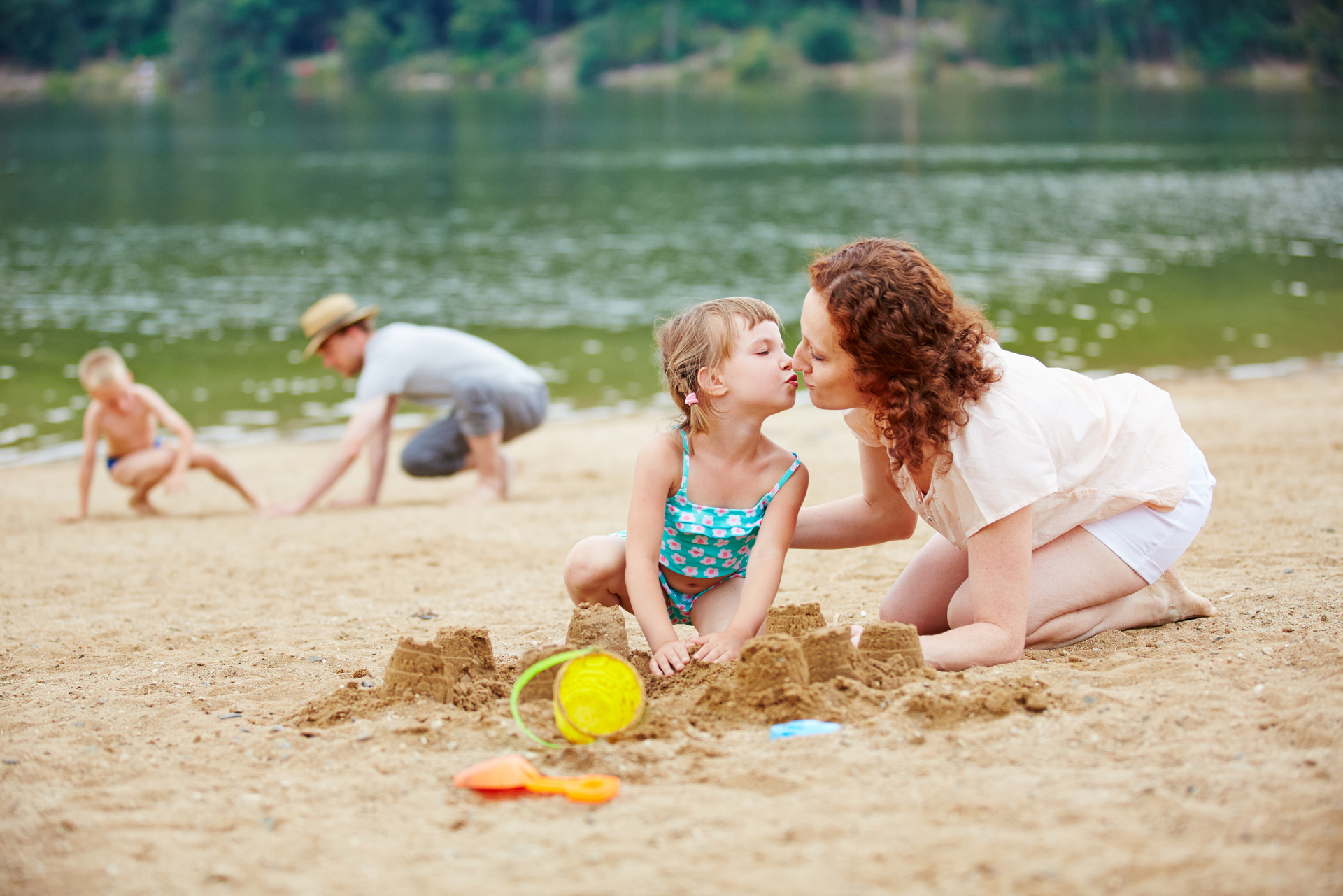 Eine Frau küsst ein kleines Mädchen auf die Wange, während sie am Strand eine Sandburg bauen.