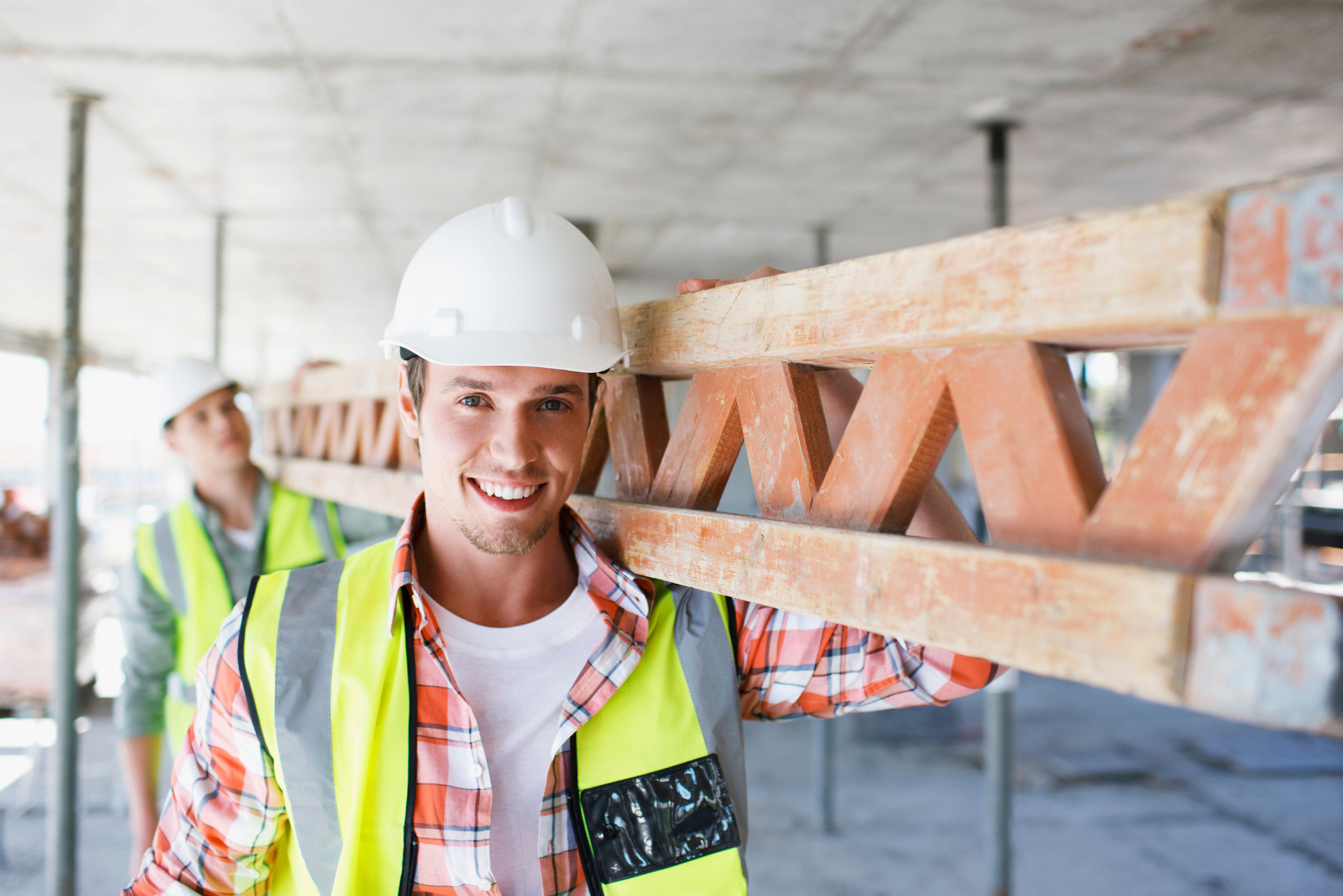 Ein Bauarbeiter trägt einen Holzbalken auf seinen Schultern.